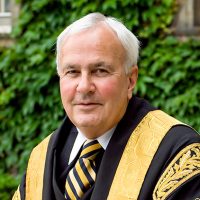 Chancellor David Peterson in front of Simcoe Hall, wearing his black and gold ceremonial robes and a matching striped tie.