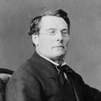The Honourable Edward Blake sitting in a chair in glasses and a suit.