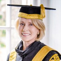 Chancellor Rose Patten standing by a window in her office wearing her ceremonial black and gold robes and mortar board.